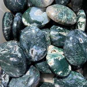 Op de afbeelding: Een verzameling groene mosagaat-tumbled stones. De stenen zijn glad en gepolijst, met een verscheidenheid aan groene, witte en grijze patronen.