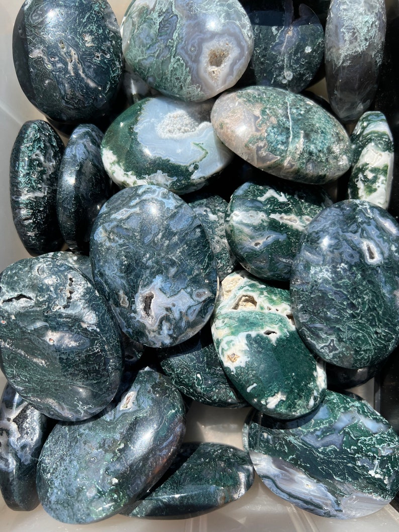Op de afbeelding: Een verzameling groene mosagaat-tumbled stones. De stenen zijn glad en gepolijst, met een verscheidenheid aan groene, witte en grijze patronen.