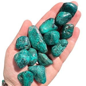 May include: A collection of polished, teal-colored stones with a mottled texture. The stones vary in size and shape, with a mix of rounded and irregular forms. The overall color is a deep teal with darker, almost black, inclusions. These stones are likely used for decorative or metaphysical purposes.