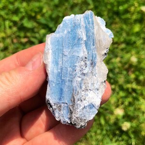 May include: A blue and white crystal with a rough, natural texture. The crystal has a layered, striated appearance.