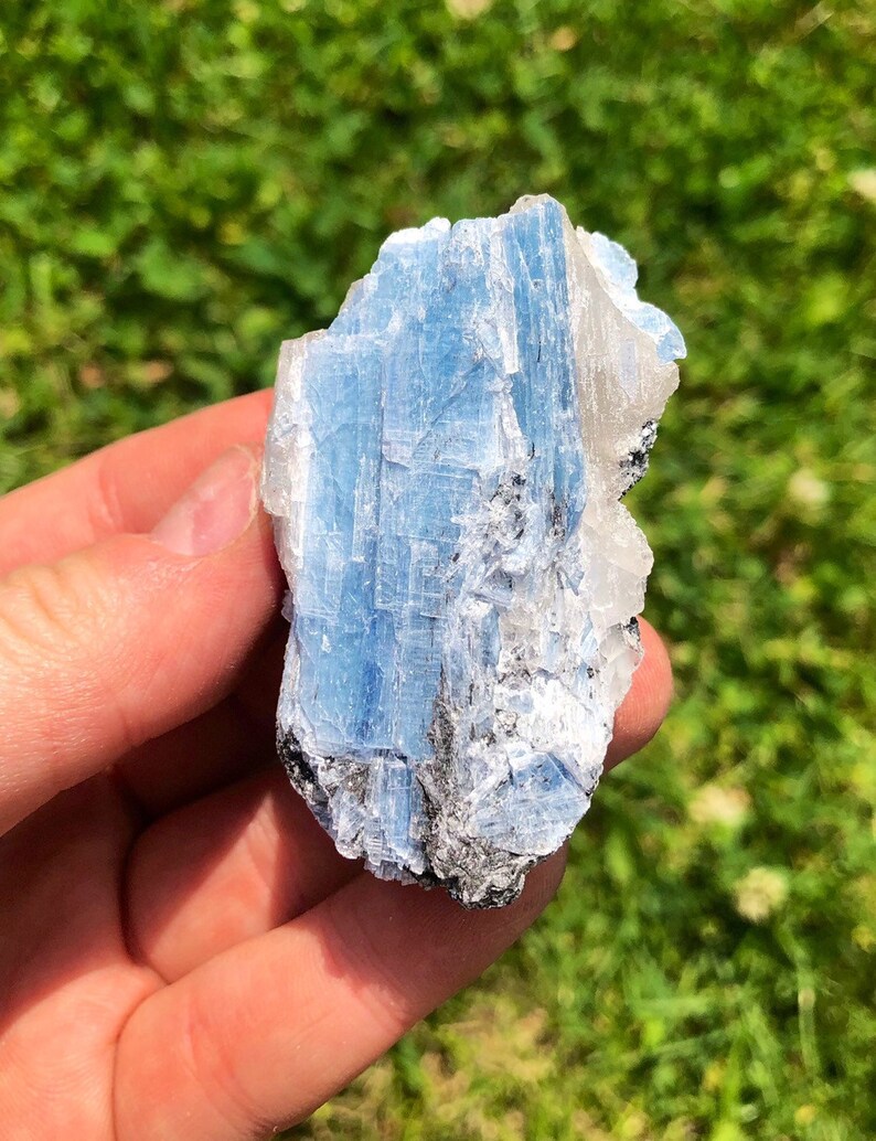 May include: A blue and white crystal with a rough, natural texture. The crystal has a layered, striated appearance.