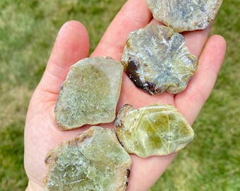 May include: Five green and brown, irregularly shaped, polished, natural gemstone crystals. The crystals have a translucent, glassy appearance.