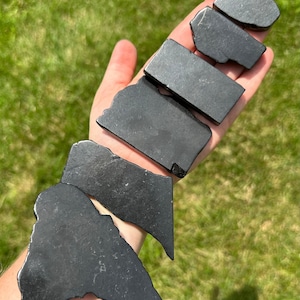 May include: A collection of seven black obsidian stones of varying sizes and shapes. The stones are smooth and polished, with a dark, glossy finish.