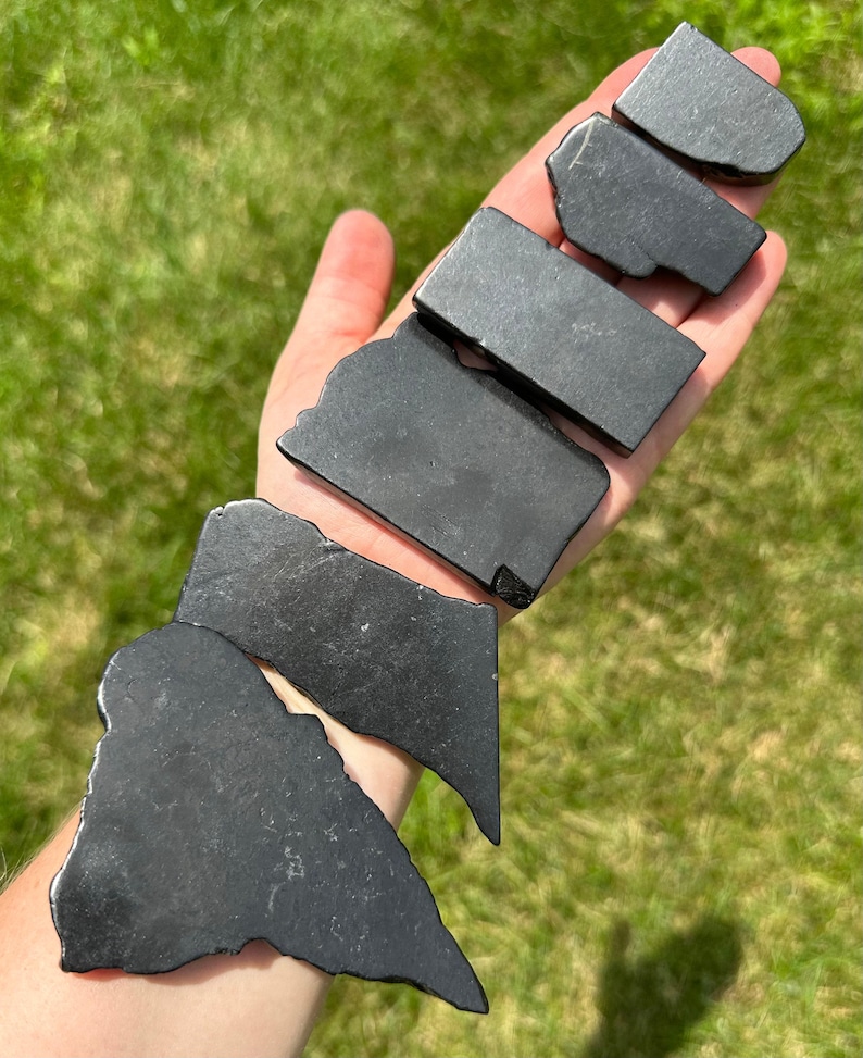 May include: A collection of seven black obsidian stones of varying sizes and shapes. The stones are smooth and polished, with a dark, glossy finish.
