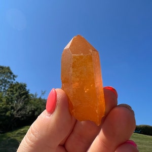 May include: A large, orange, crystal point with a pointed tip and a smooth, polished surface.