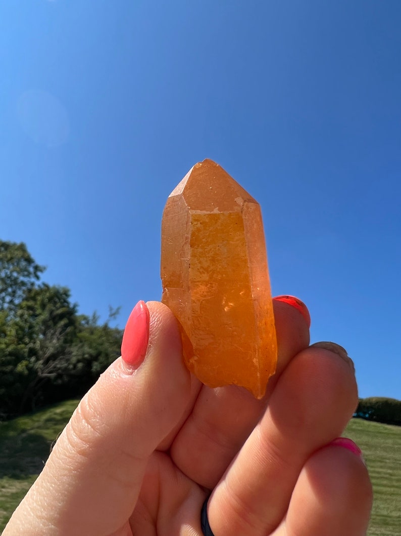 May include: A large, orange, crystal point with a pointed tip and a smooth, polished surface.