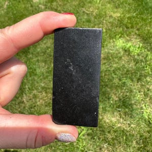May include: A black rectangular stone with a smooth surface. The stone is about 2 inches long and 1 inch wide.