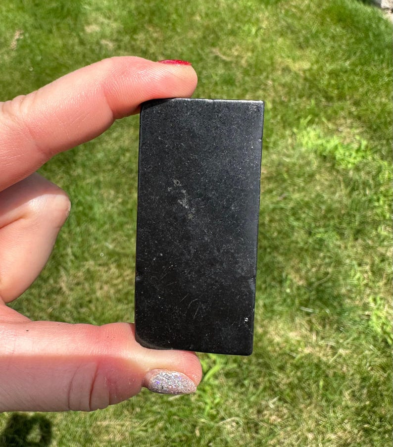 May include: A black rectangular stone with a smooth surface. The stone is about 2 inches long and 1 inch wide.