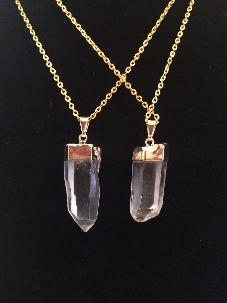Puede incluir: Dos collares de cadena dorada con colgantes de punta de cristal de cuarzo transparente. Los colgantes est&aacute;n engastados en metal dorado.