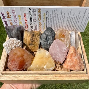 May include: A wooden box filled with various crystals and stones, including amethyst, citrine, carnelian, black tourmaline, clear quartz, orange calcite, and yellow calcite. Each stone is labeled with its name.