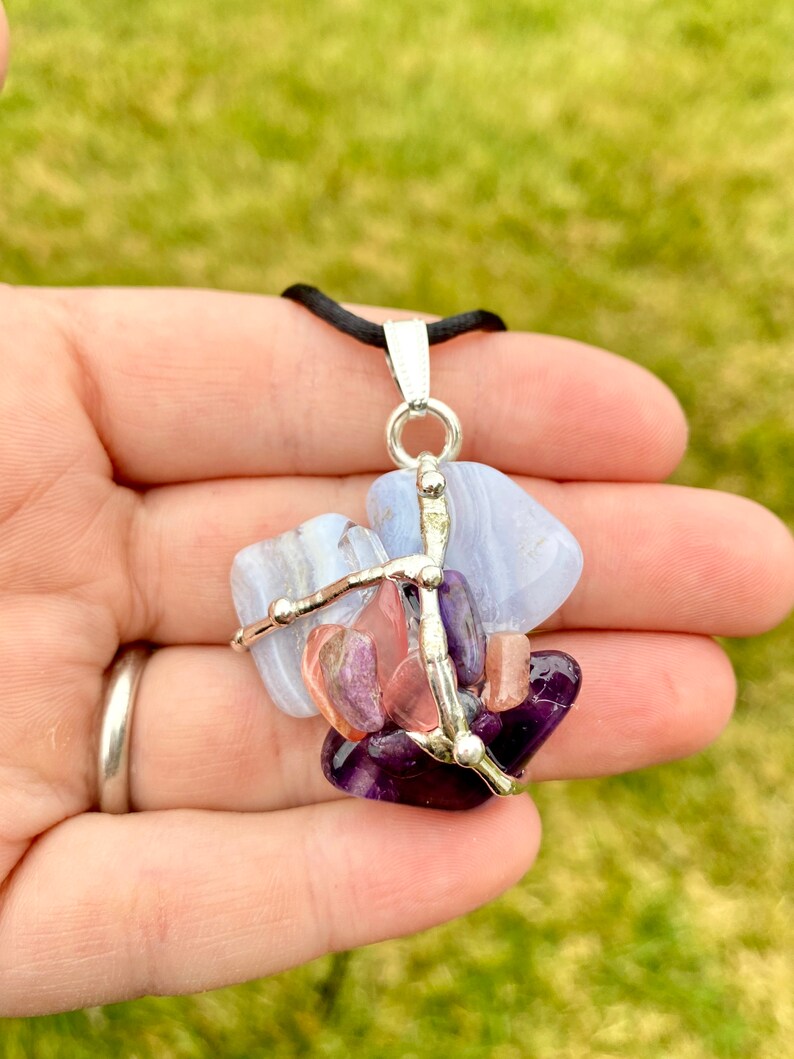 May include: A silver wire wrapped pendant featuring a variety of semi-precious stones, including blue lace agate, amethyst, and rose quartz. The pendant is suspended from a black cord.