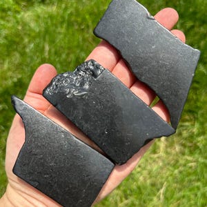 May include: Three black obsidian stones, each with a unique shape and texture. The stones are smooth and polished, with a deep black color.