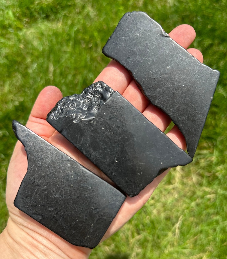 May include: Three black obsidian stones, each with a unique shape and texture. The stones are smooth and polished, with a deep black color.