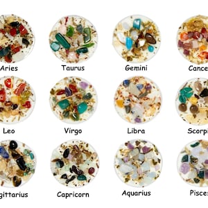 May include: Twelve small white candles with different colored crystals and herbs embedded in the wax. Each candle is labeled with a zodiac sign: Aries, Taurus, Gemini, Cancer, Leo, Virgo, Libra, Scorpio, Sagittarius, Capricorn, Aquarius, and Pisces.