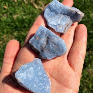May include: Three blue celestite crystal stones, each with a unique shape and texture. The stones are smooth and have a light blue color.