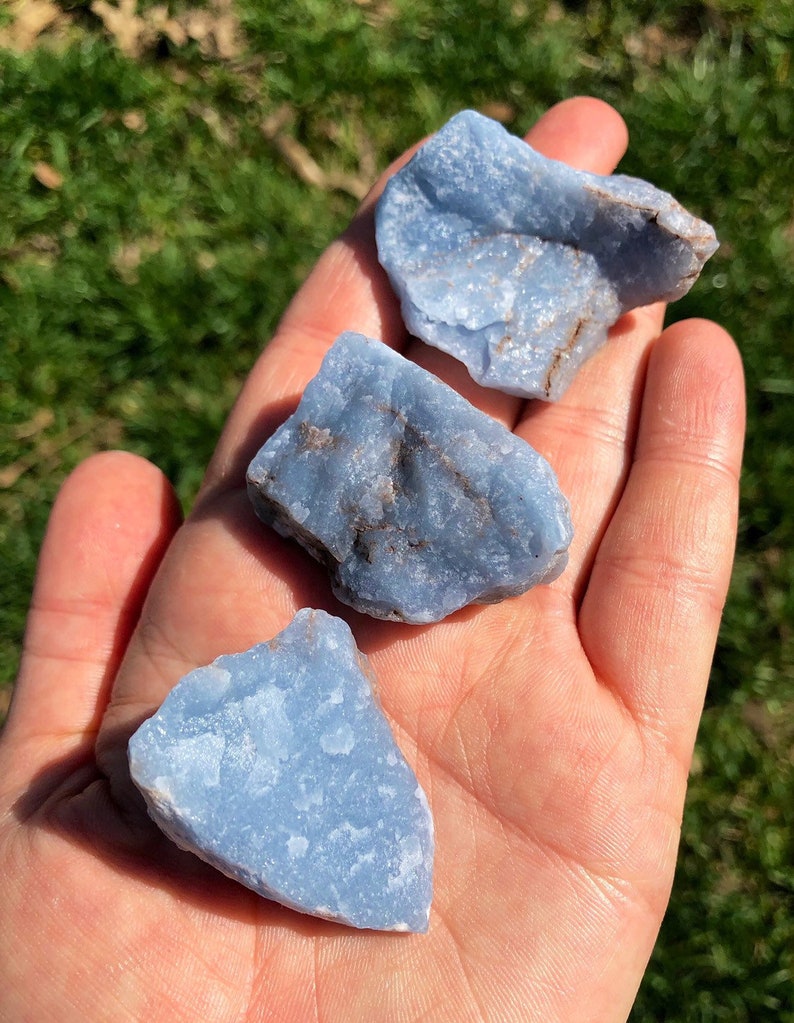 May include: Three blue celestite crystal stones, each with a unique shape and texture. The stones are smooth and have a light blue color.