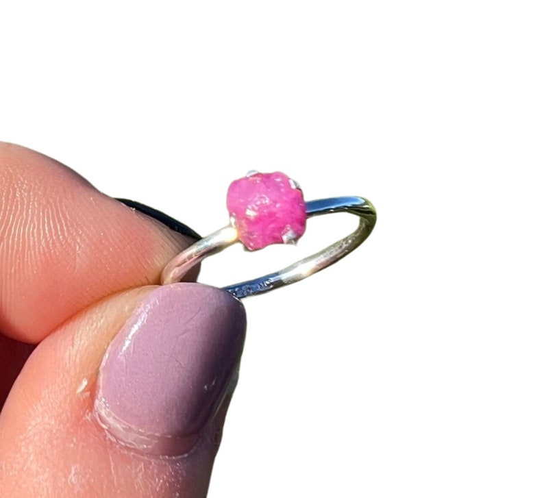 May include: A silver ring with a pink, raw ruby gemstone set in the center.