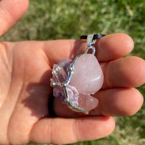 May include: A silver wire wrapped pendant featuring a pink rose quartz, amethyst, and clear quartz crystal. The pendant is on a black cord.