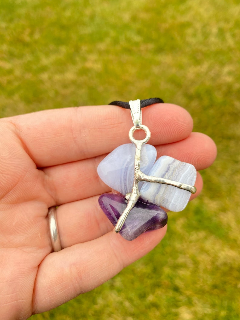 May include: A silver wire wrapped pendant featuring a blue agate and amethyst stone. The stones are held together by a silver wire that forms a branch-like design.