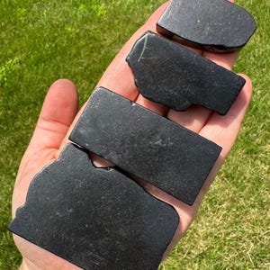 May include: Four black obsidian stones of varying sizes and shapes, arranged in a stack on a hand.