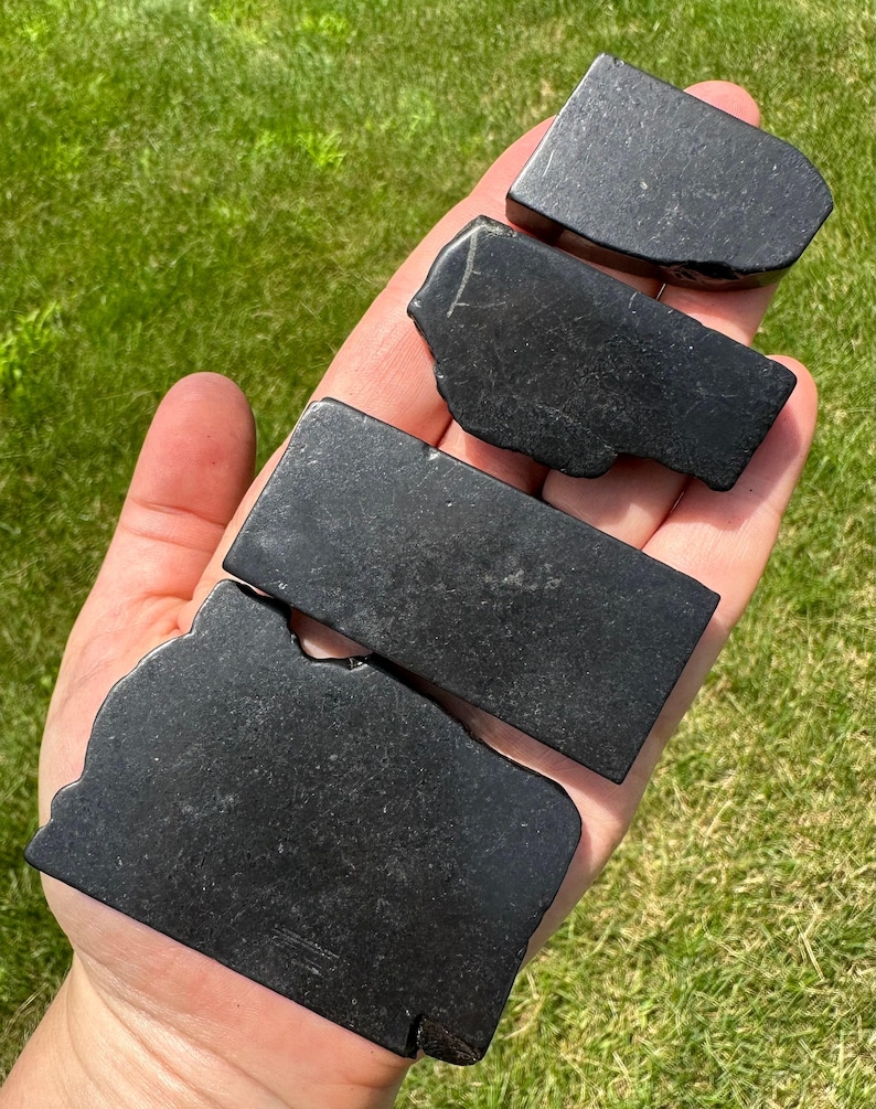 May include: Four black obsidian stones of varying sizes and shapes, arranged in a stack on a hand.