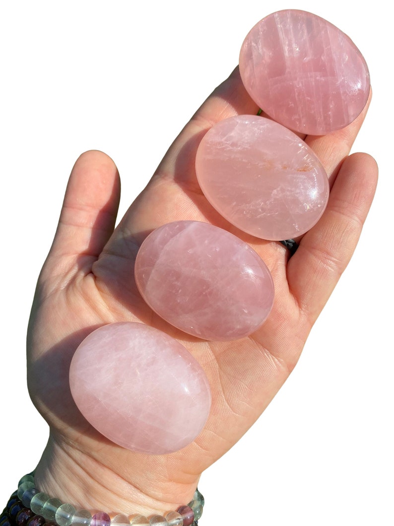 Pu&ograve; includere: Quattro pietre di quarzo rosa lisce e levigate di diverse dimensioni. Le pietre sono di colore rosa pallido e hanno un aspetto naturale leggermente nuvoloso.