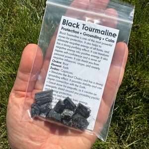 May include: A small plastic bag containing black tourmaline crystals. The bag has a label that reads "Black Tourmaline Protection. Grounding. Calm" and describes the properties of the crystals.