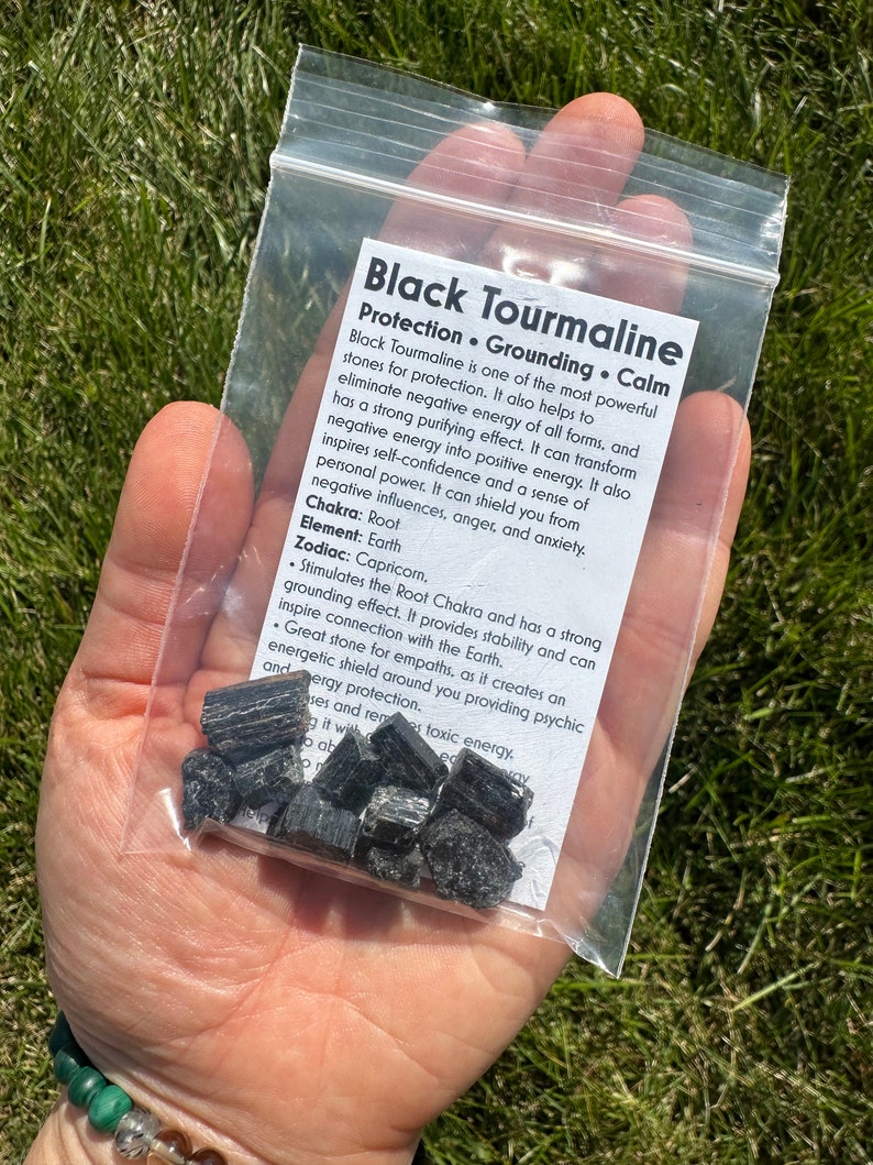 May include: A small plastic bag containing black tourmaline crystals. The bag has a label that reads "Black Tourmaline Protection. Grounding. Calm" and describes the properties of the crystals.