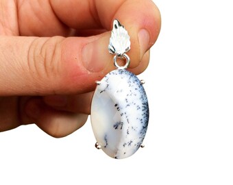Puede incluir: Un colgante de plata con una piedra de ópalo dendrítico blanco y negro con una anilla de ala de plata.