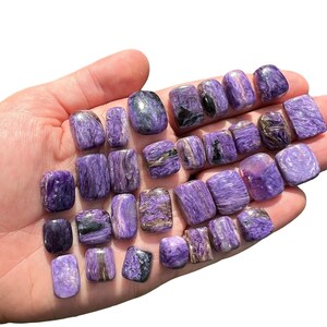 May include: A collection of 20 purple and silver apophyllite tumbled stones. The stones are smooth and polished, with a variety of shapes and sizes.