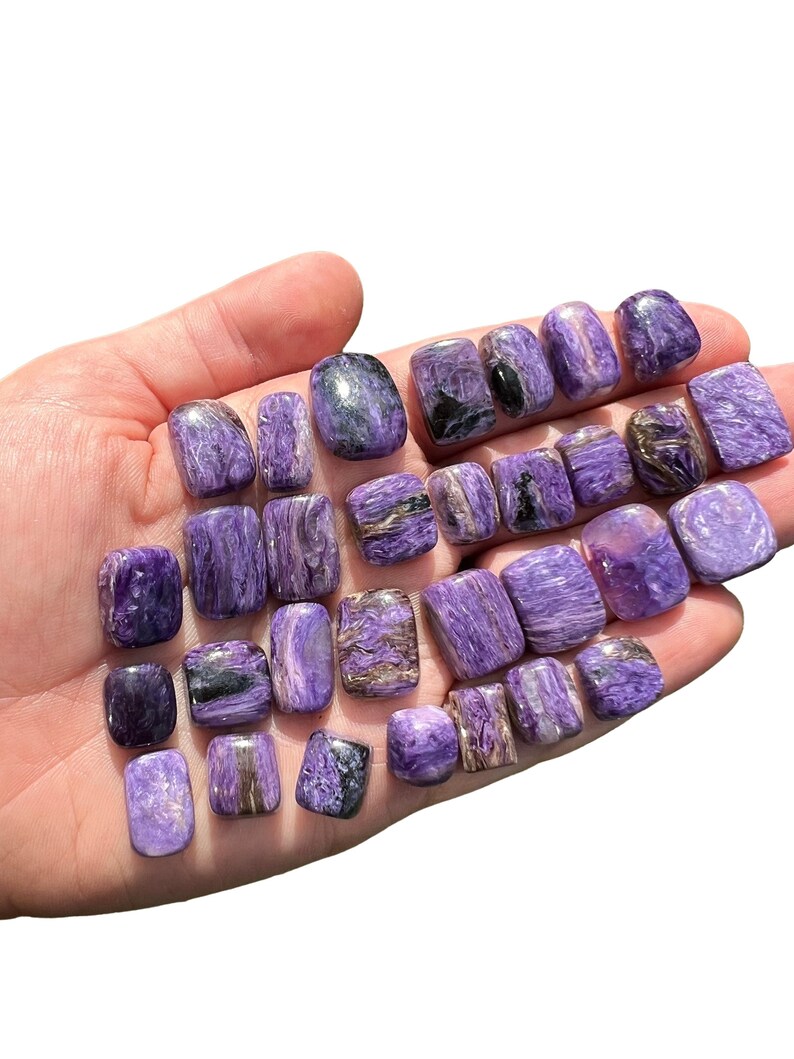 May include: A collection of 20 purple and silver apophyllite tumbled stones. The stones are smooth and polished, with a variety of shapes and sizes.
