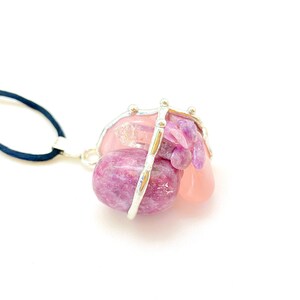 May include: A silver wire cage pendant necklace with pink and purple gemstones. The necklace is made with a black cord.
