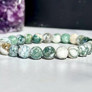 Könnte beinhalten: Ein Armband aus grünem und weißem Achat mit runden Perlen. Das Armband besteht aus natürlichen Steinen und hat ein einzigartiges Muster.