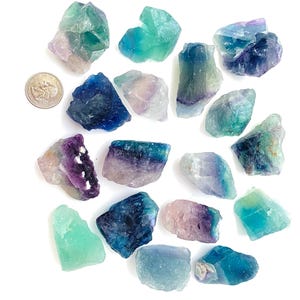 Puede incluir: Una colecci&oacute;n de 17 cristales de fluorita en varios tonos de verde, azul y morado. Los cristales son &aacute;speros y tienen un aspecto natural sin pulir.