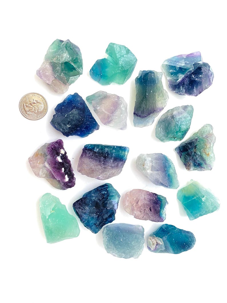 Puede incluir: Una colecci&oacute;n de 17 cristales de fluorita en varios tonos de verde, azul y morado. Los cristales son &aacute;speros y tienen un aspecto natural sin pulir.