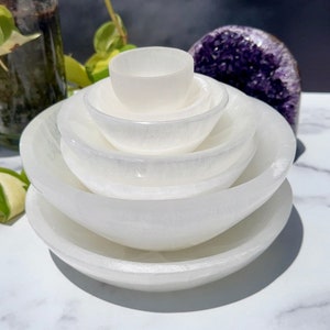 Pu&ograve; includere: Un set di cinque ciotole di selenite bianca, impilate in ordine decrescente di dimensioni, con la ciotola pi&ugrave; piccola in cima. Le ciotole sono lisce e hanno una leggera lucentezza iridescente.