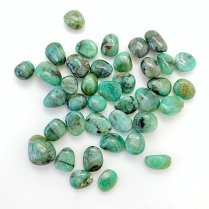 Op de afbeelding: Een verzameling van gepolijste smaragdgroene stenen met zwarte en witte insluitsels. De stenen zijn glad en gepolijst en liggen los op een witte achtergrond.