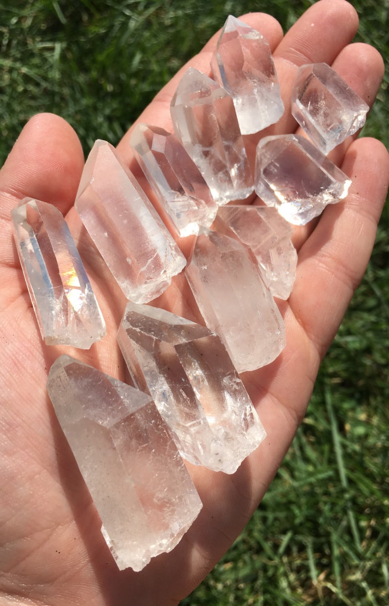 May include: A collection of clear quartz crystal points, also known as rock crystals, in various sizes and shapes. The crystals are arranged in a hand, showcasing their natural beauty and clarity.