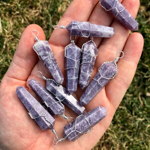 May include: A collection of ten purple lepidolite crystal points wrapped in silver wire. Each point has a silver loop at the top for hanging.