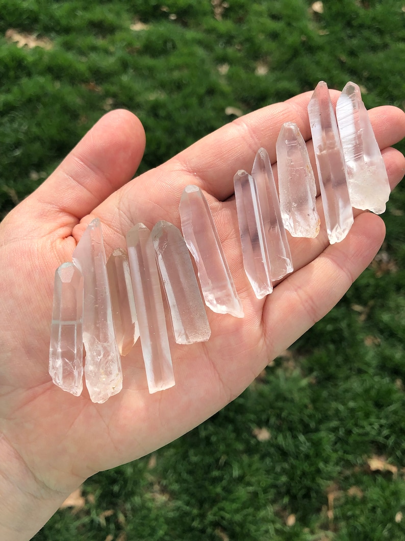 May include: A collection of clear quartz crystal points, also known as rock crystals, displayed in a hand. The points are various sizes and shapes, with some being longer and thinner than others.