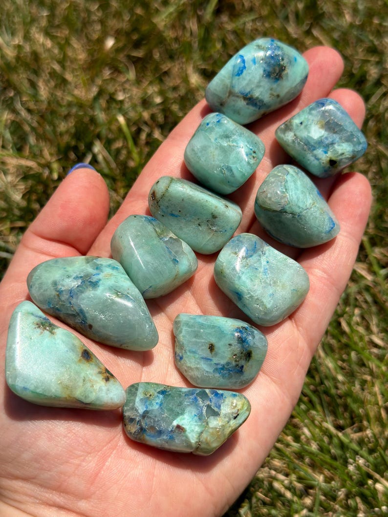 May include: A collection of ten tumbled blue and green chrysocolla stones. The stones are smooth and polished, with a variety of shapes and sizes.
