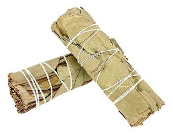 Puede incluir: Dos manojos de hojas de salvia secas atadas con cuerda blanca. La salvia es de color marrón claro y las hojas están apretadas.
