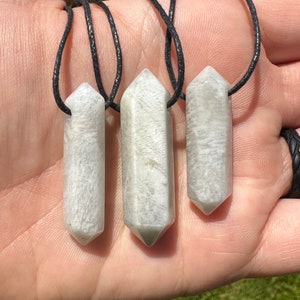May include: Three white crystal point pendants on black cords. The crystals are long and slender with a pointed tip.
