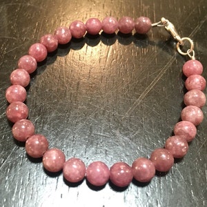 K&ouml;nnte beinhalten: Ein Armband aus rosa Lepidolith-Edelsteinen mit einem silbernen Verschluss.