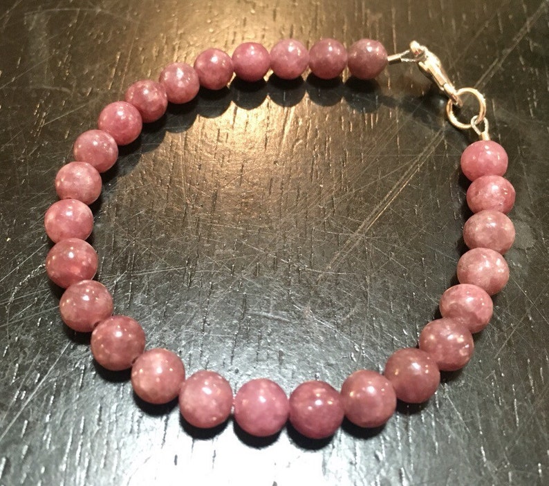 K&ouml;nnte beinhalten: Ein Armband aus rosa Lepidolith-Edelsteinen mit einem silbernen Verschluss.