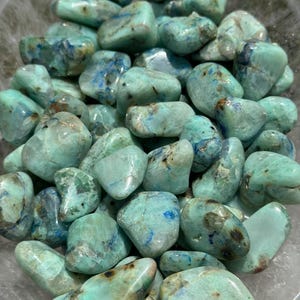 May include: A collection of tumbled green and blue chrysocolla stones. The stones are smooth and polished, with a variety of shapes and sizes.