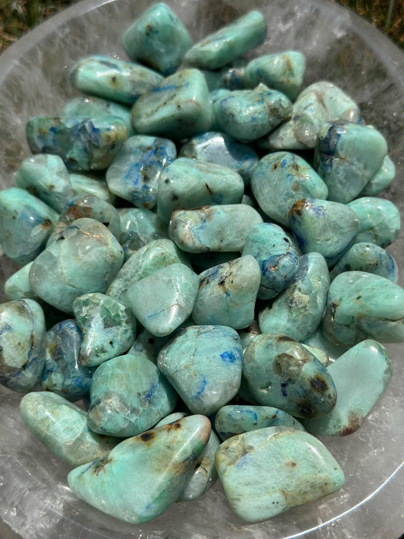 May include: A collection of tumbled green and blue chrysocolla stones. The stones are smooth and polished, with a variety of shapes and sizes.