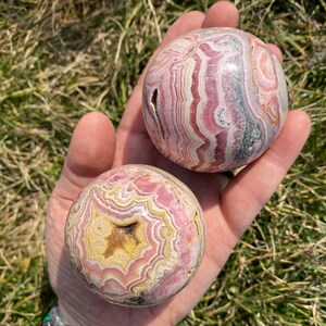 May include: Two pink and white striped spheres of polished pink and white banded agate. The spheres are smooth and have a natural, organic look.