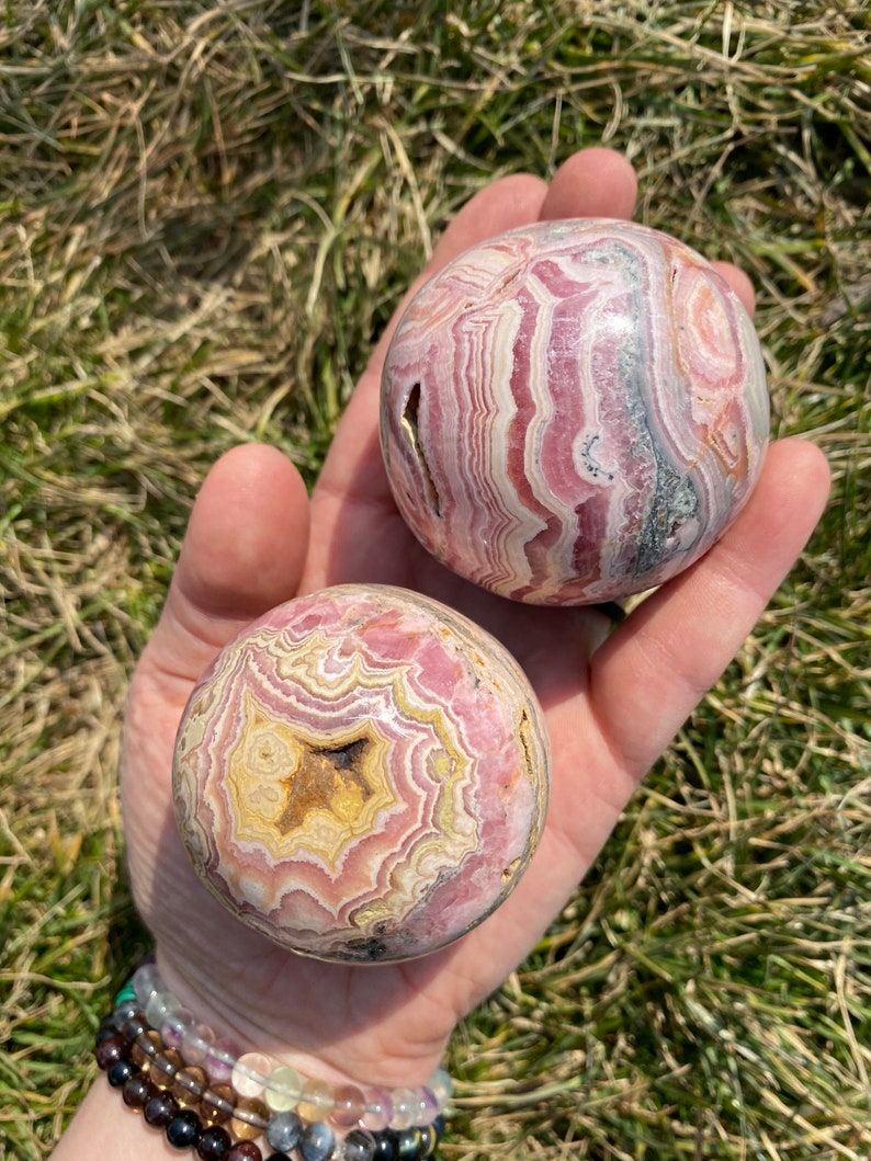 May include: Two pink and white striped spheres of polished pink and white banded agate. The spheres are smooth and have a natural, organic look.