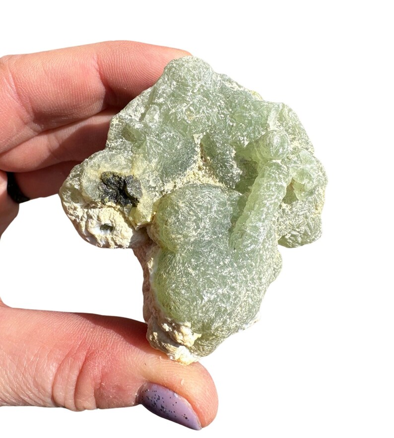 Puede incluir: Un c&uacute;mulo de cristales de prehnita verde con una superficie rugosa y texturizada. El cristal es de color verde claro y tiene un aspecto natural y terroso.